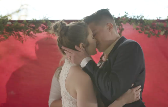 Marlee & Tabatha Castillo share a kiss at their wedding where Sara Cunningham served as a “stand-in mom” for Tabatha, photo courtesy the artist.
